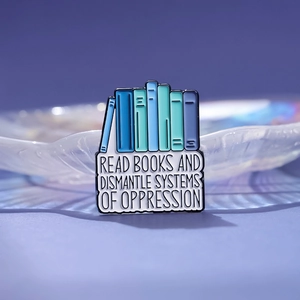 Enamel book brooch featuring Read Books and Dismantle Systems of Oppression quote