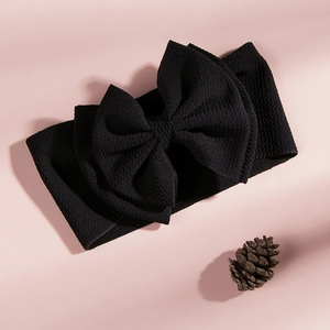 Close-up of black waffle texture baby headband with a large bow on pink background