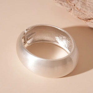 Detail of wide matte silver metal cuff bracelet featuring a brushed texture finish