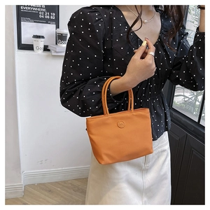 Détail d'un sac seau en nylon orange avec logo m porté par un mannequin dans un café