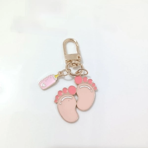 Detail of pink enamel baby feet and milk bottle charms on a golden metal keychain