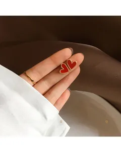 Macro detail of red enamel heart earring with gold border held between fingers