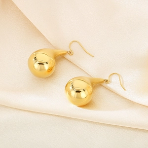 Polished gold hollow teardrop earrings on elegant beige silk fabric background