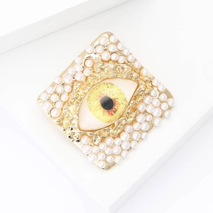 Detail of square gold eye brooch with yellow iris and faux pearl embellishments