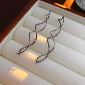 Gros plan de boucles d'oreilles noires en métal ondulé sur un coussin blanc