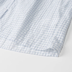 Detail of light blue gingham seersucker fabric and stitching on the shirt hemline