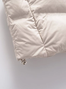 Detail of adjustable metal drawstring toggle on beige quilted padded vest