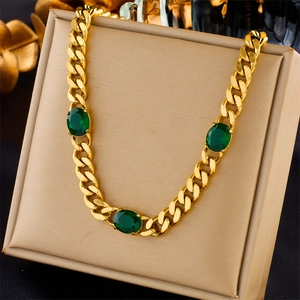 Golden Cuban chain necklace with three oval green gemstones on a beige jewelry stand