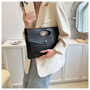 Detail of black crocodile texture envelope clutch bag with cut-out handle and gold button