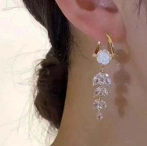 Close-up of gold flower earrings with marquise-cut zircon drops worn on a model