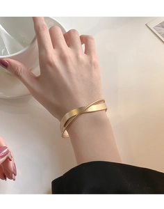 Dettaglio di un bracciale rigido incrociato oro opaco minimalista indossato al polso
