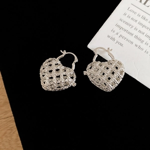 Macro detail of silver hollow mesh heart hoop earrings on a black velvet background