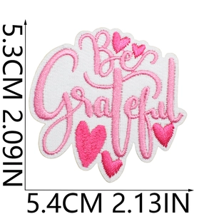 Macro shot of pink Be Grateful embroidered patch with heart motifs and measurements