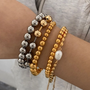 Detail of stacked stainless steel beaded bracelets with a white pearl charm on wrist