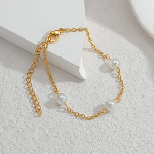 Detail of gold chain bracelet with three white pearls on minimalist white stone