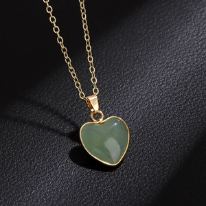 Detailed close-up of a green heart crystal pendant with gold plating on black texture