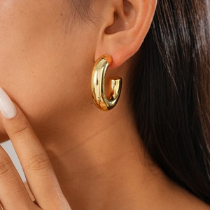 Close-up of a chunky golden C-shaped hoop earring with a metallic finish on a model