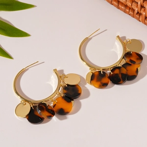 Close-up of golden C-shaped hoop earrings with leopard resin and metallic disc charms