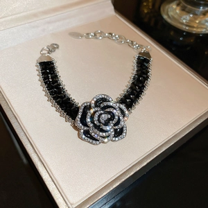 Close-up of black camellia bracelet with crystals and woven chain in a jewelry box