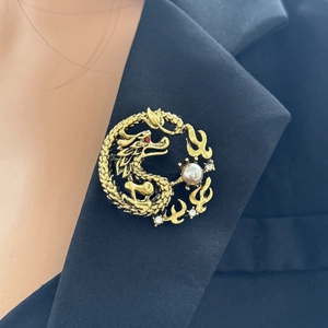 Detailed close-up of a golden Chinese dragon brooch with pearl and rhinestones on black suit