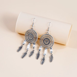 Close-up of bohemian dreamcatcher feather earrings with beads on a beige pedestal
