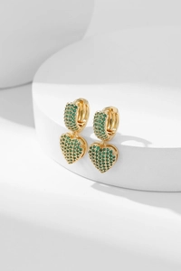 Detail of gold heart earrings featuring green micro-pave cubic zirconia on stand