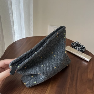 Detail showing thick gray knitted makeup bag texture with colorful speckles on a wooden table