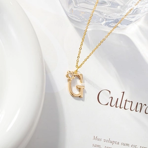 Detailed view of a gold G-letter necklace with a zircon-inlaid flower on a refined chain