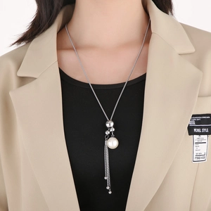 Dettaglio della collana lunga con nappe e pendente di perla bianca su un elegante blazer beige