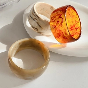Three-piece set of wide resin bangles in marble and amber colors on a ceramic dish