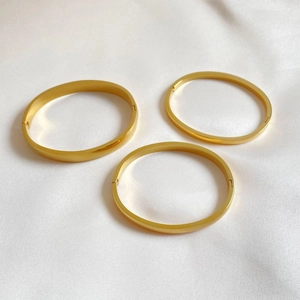 Detailed view of three minimalist polished gold bangles on elegant white silk fabric