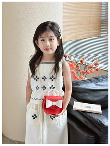 Detail of red kids crossbody bag with white bow, pearl handle and gold chain strap