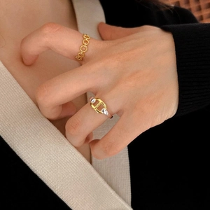 Detail of gold chain texture and two-tone pig nose buckle rings worn on fingers