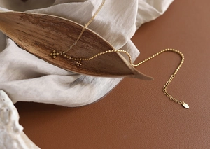 Detail of 18K gold-plated beaded cross necklace featuring extension chain and round tag