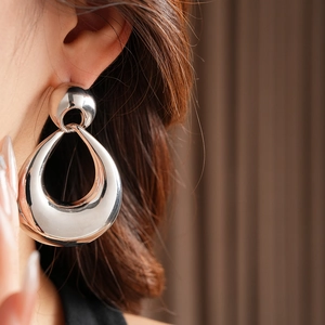 Side close-up of large silver teardrop geometric earrings with a polished metallic finish