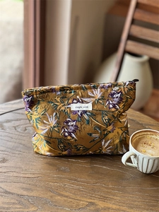 Detailed embroidery of purple flowers on a yellow cosmetic bag near a coffee cup