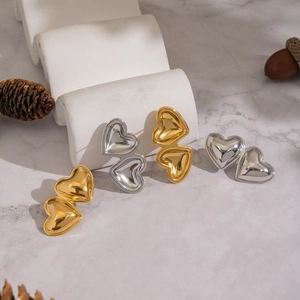Minimalist gold and silver heart studs on a white wave stand with marble background