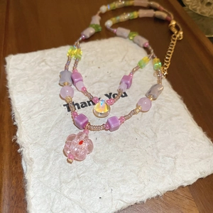 Detail view of colorful glass beads necklace featuring a pink flower charm and gold clasp