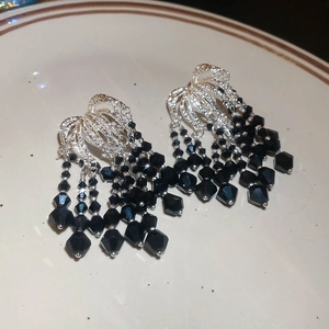Detailed view of silver stud earrings with cascading black crystal beaded tassels on ceramic