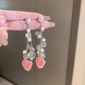 Close-up of long pearl tassel earrings with pink plush heart pendant and golden chain