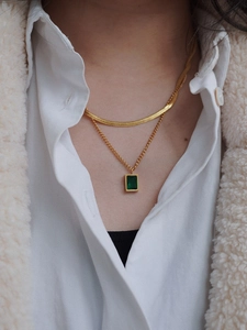 Close-up of double-layer gold necklace with emerald pendant and flat snake chain on neck