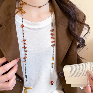 Detail of long crystal beaded necklace with bows on model wearing a brown blazer