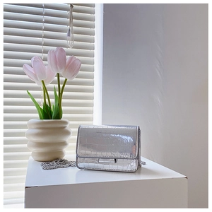 Silver crocodile texture mini square bag with metal chain strap on a minimalist white table