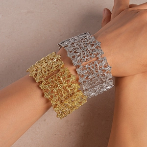 Gros plan de bracelets manchettes larges ajourés en or et argent sur les bras