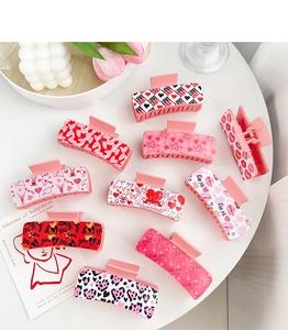 Flat lay of pink and red heart-patterned hair claws on a white table for Valentine's day