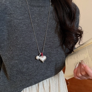 Macro shot of silver beaded chain necklace with matte heart pendant on grey sweater