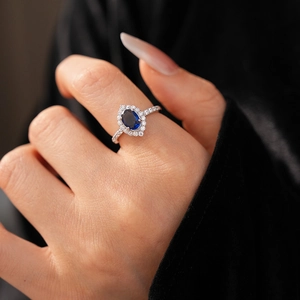 Macro detail of oval blue gemstone ring with zircon halo on model's hand