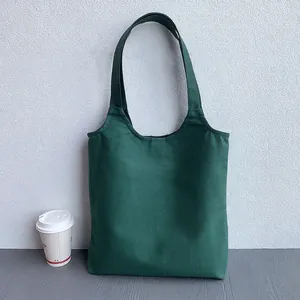 Detail view of a dark green canvas tote bag with a coffee cup for size scale