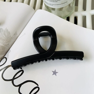 Matte black oversized shark hair claw clip with cross-wrap design on white book background