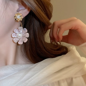 Close-up of pink flower earrings with pearls and gold petals worn on model ear